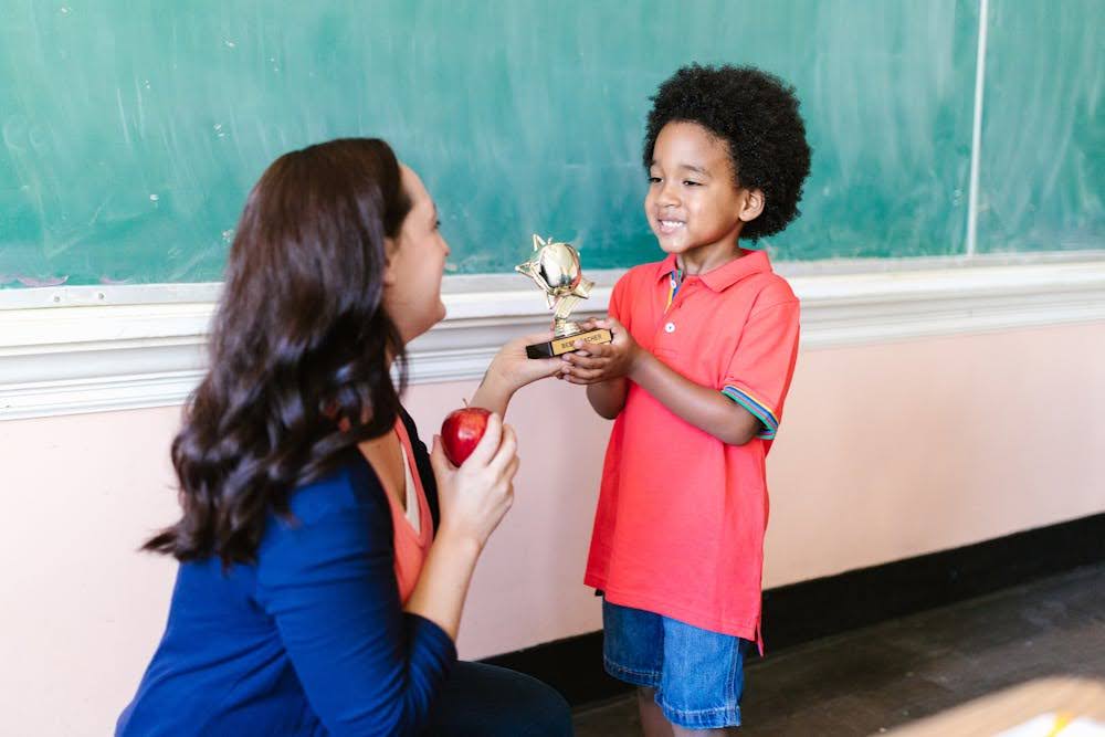 A teacher handing an award trophy to an elementary school student